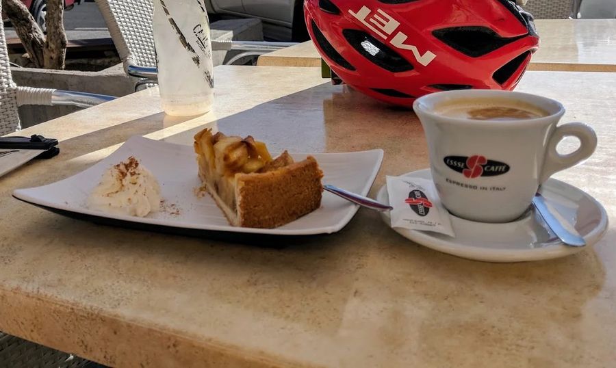 Apple cake with cream, a coffee, a water bottle and a red helmet on a sunny terrace table