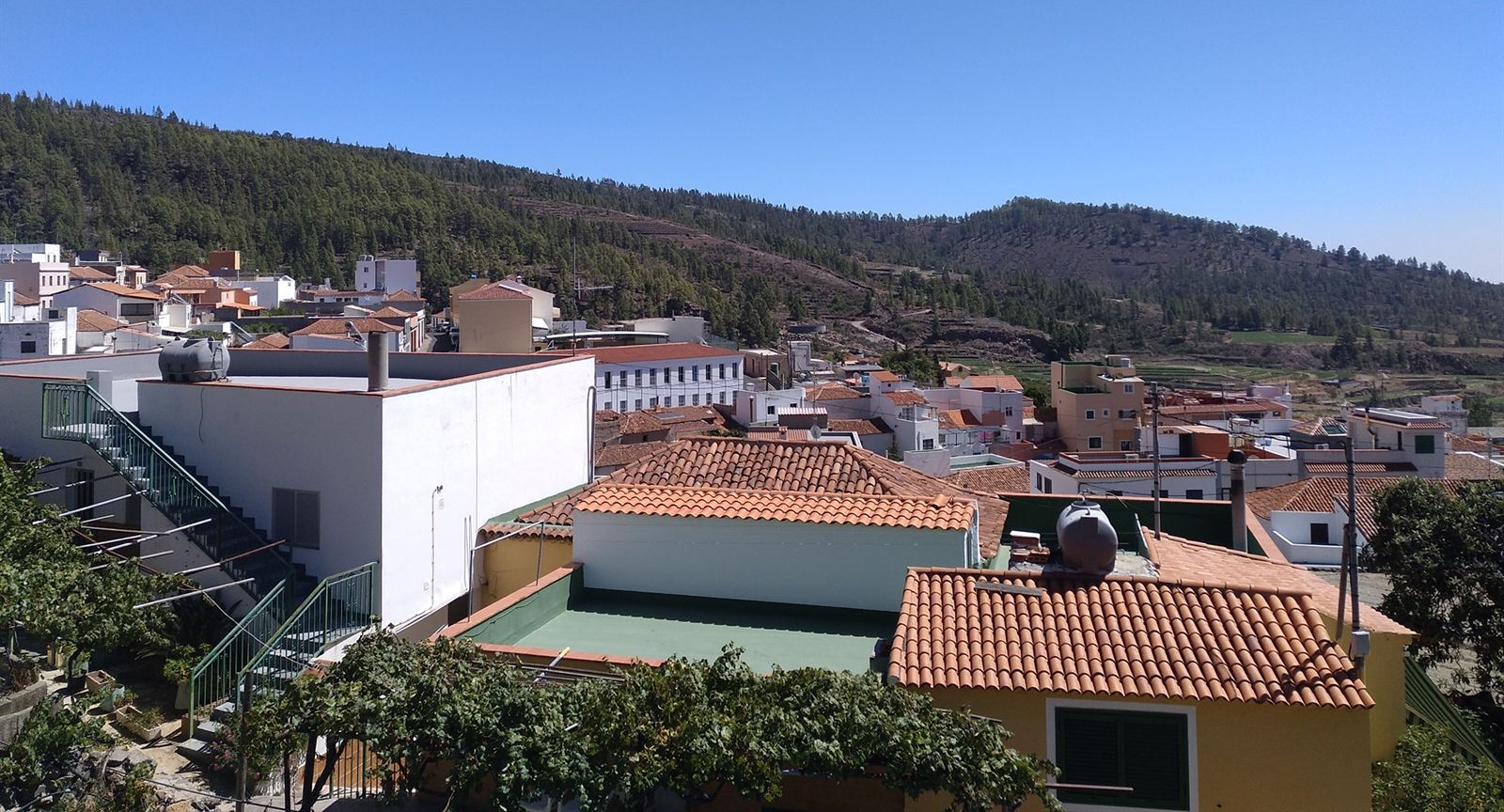 Terracotta rooftops of Vilaflor with pine-covered hills behind under a clear blue sky